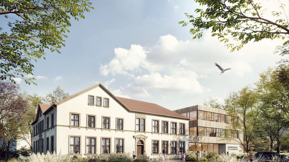 Eine Schule mit einem alten weißen Gebäude und einem modernen Holzanbau, umgeben von grünen Bäumen und bepflanzten Gärten unter blauem Himmel.